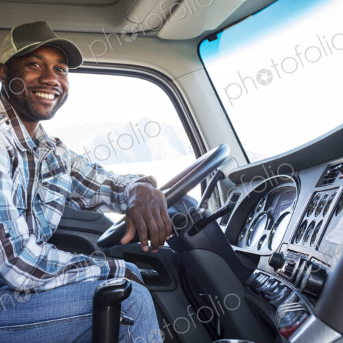 Black man truck driver in the cab of his commercial truck.