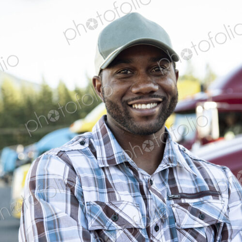 Black man truck driver near his truck parked in a parking lot at a truck stop Black man truck driver near his truck parked in a parking lot at a truck stop