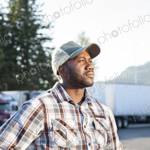 Black man truck driver near his truck parked in a parking lot at a truck stop Black man truck driver near his truck parked in a parking lot at a truck stop