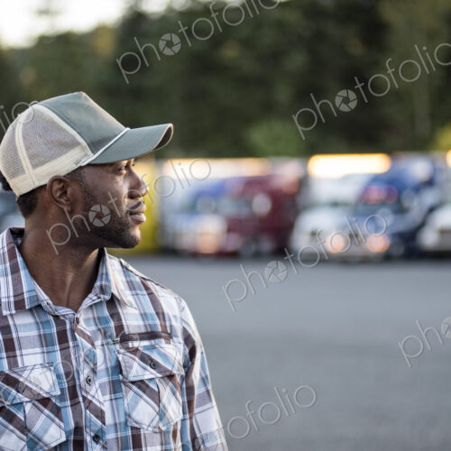 Black man truck driver near his truck parked in a parking lot at a truck stop Black man truck driver near his truck parked in a parking lot at a truck stop