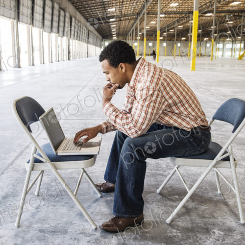 Black man working on lap top computer in front of loading dock doors in a new warehouse. Black man working on lap top computer in front of loading dock doors in a new warehouse.