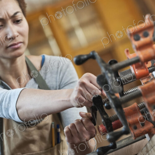 Black woman factory worker adjusting clamps while glueing a large wooden part in a…