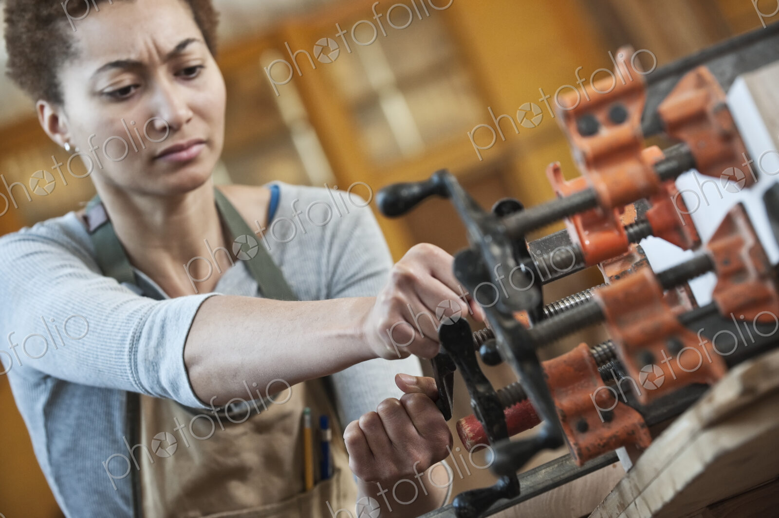 Black woman factory worker adjusting clamps while glueing a large wooden part in a…