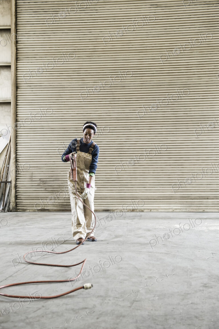 Black woman factory worker gathering tools together on the floor of a sheet metal factory.