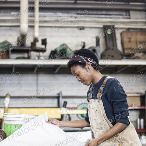 Black woman factory worker going over project plans in a sheet metal factory.