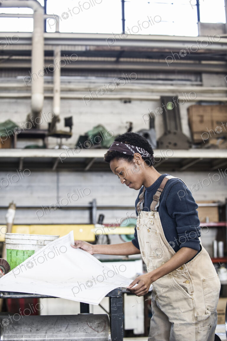 Black woman factory worker going over project plans in a sheet metal factory.