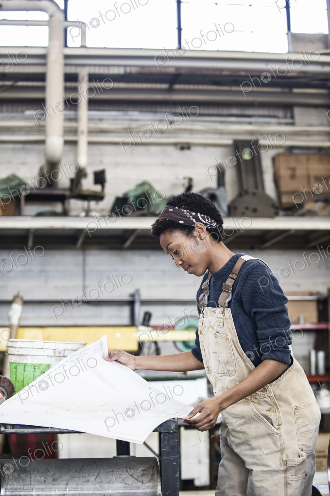 Black woman factory worker going over project plans in a sheet metal factory.