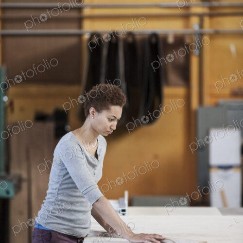 Black woman factory worker measuring wood at a work station in a woodworking factory.