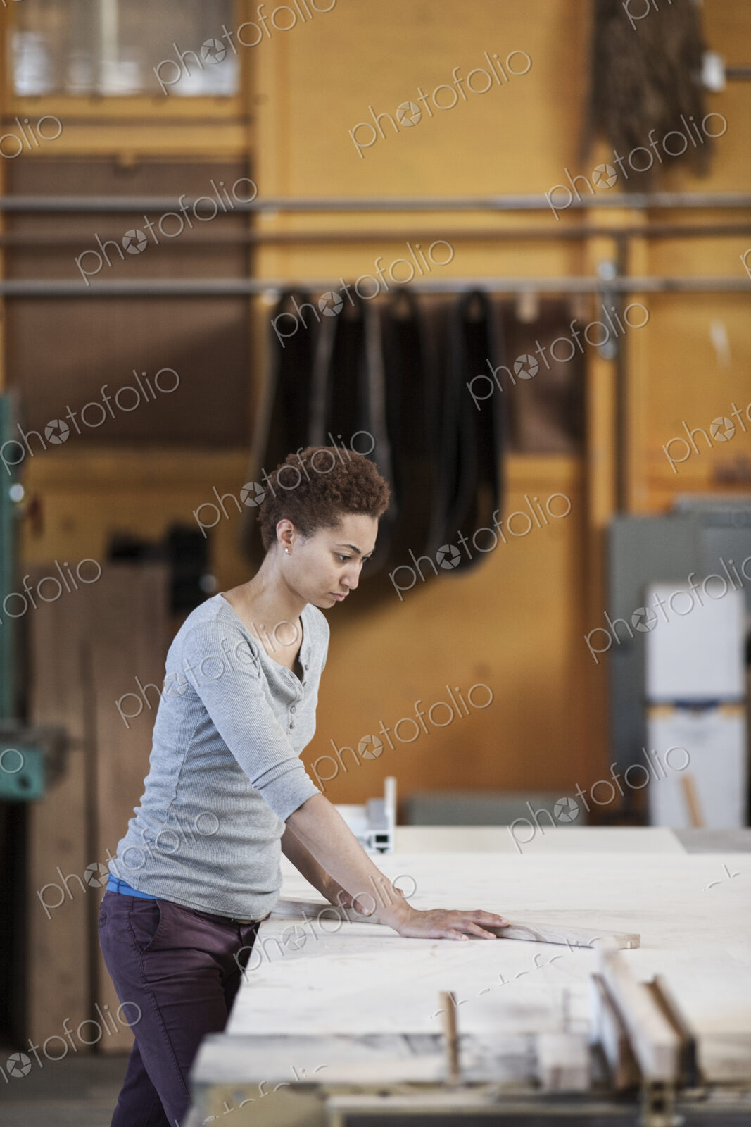 Black woman factory worker measuring wood at a work station in a woodworking factory.