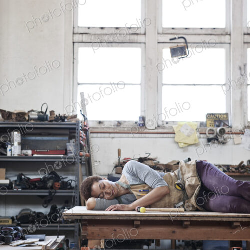 Black woman factory worker taking a nap on top of a work station in a woodworking factory.