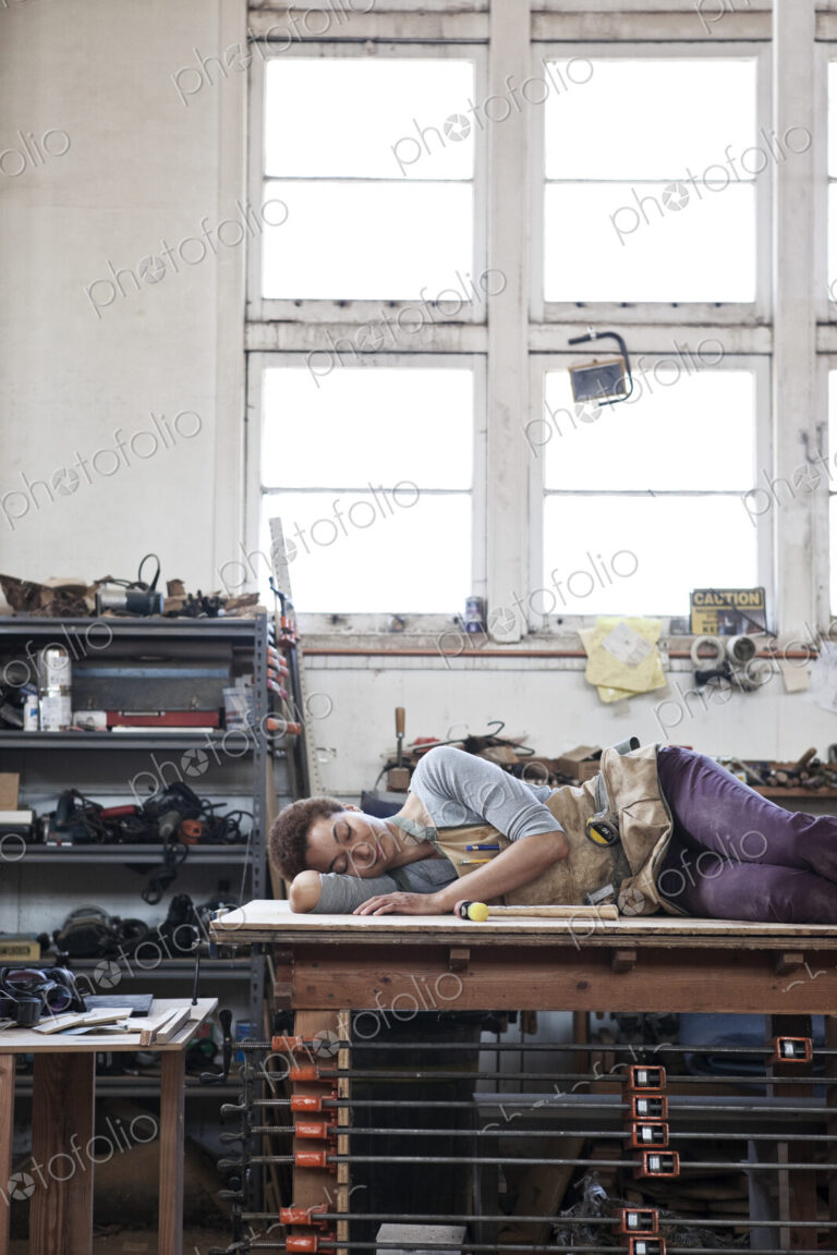 Black woman factory worker taking a nap on top of a work station in a woodworking factory.