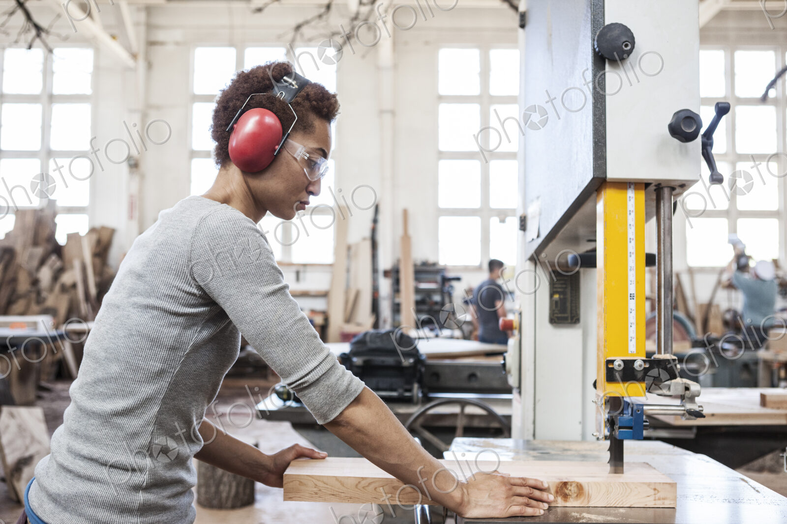 Black woman factory worker using a band saw to cut wood in a woodworking factory.