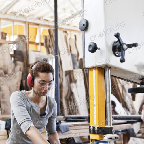 Black woman factory worker using a band saw to cut wood in a woodworking factory.