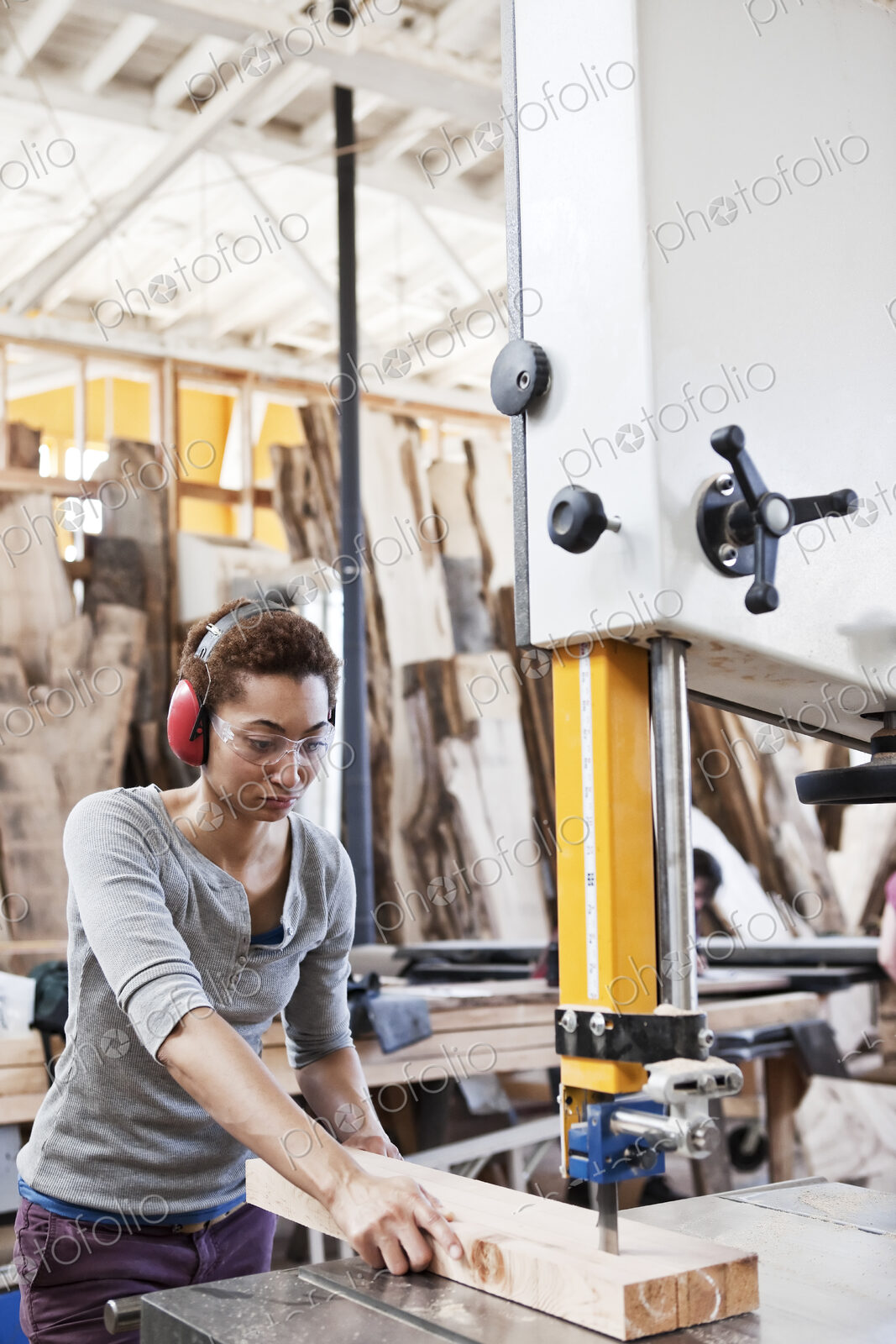 Black woman factory worker using a band saw to cut wood in a woodworking factory.
