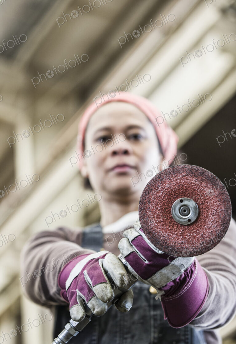 Black woman factory worker using a metal grinding tool in a sheet metal factory.