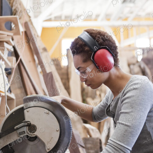 Black woman factory worker using a radial saw to cut wood in a woodworking factory.