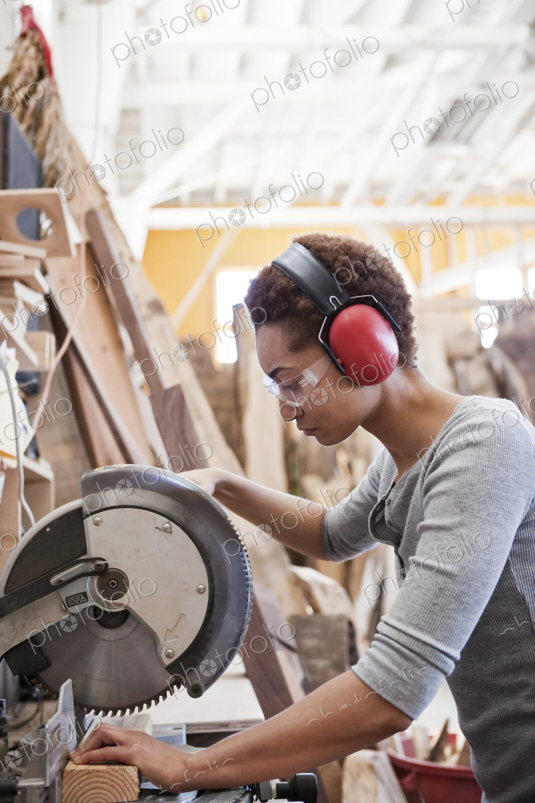 Black woman factory worker using a radial saw to cut wood in a woodworking factory.