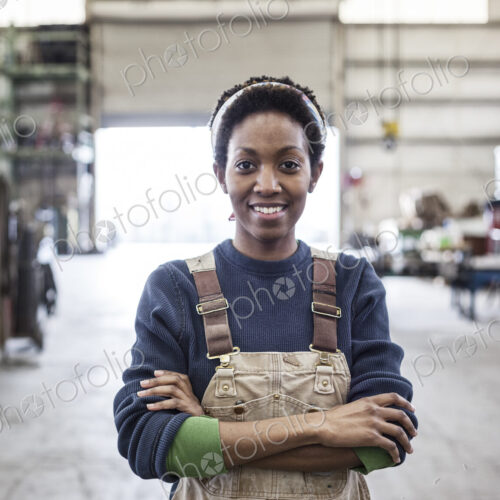 Black woman factory worker wearing coveralls in a large sheet metal factory. Black woman factory worker wearing coveralls in a large sheet metal factory.