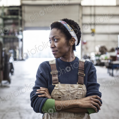 Black woman factory worker wearing coveralls in a large sheet metal factory. Black woman factory worker wearing coveralls in a large sheet metal factory.