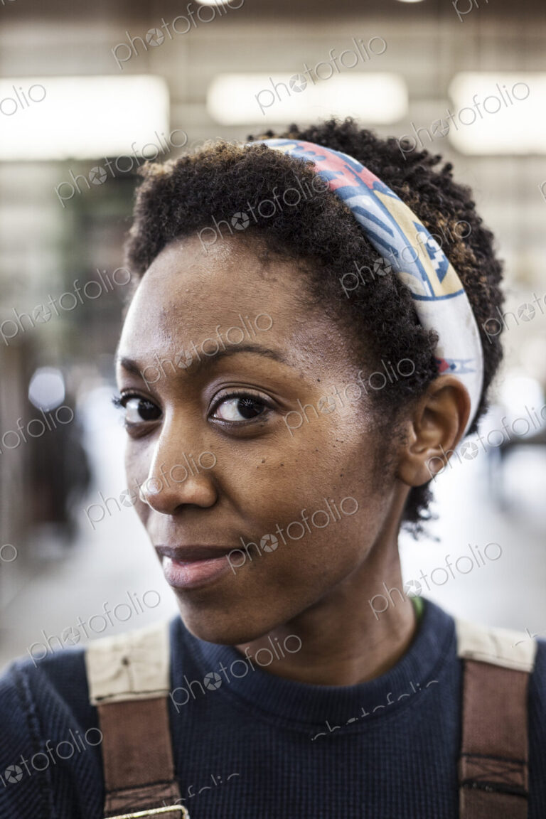 Black woman factory worker wearing coveralls in a large sheet metal factory.