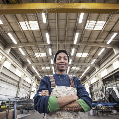 Black woman factory worker wearing coveralls in a large sheet metal factory. Black woman factory worker wearing coveralls in a large sheet metal factory.