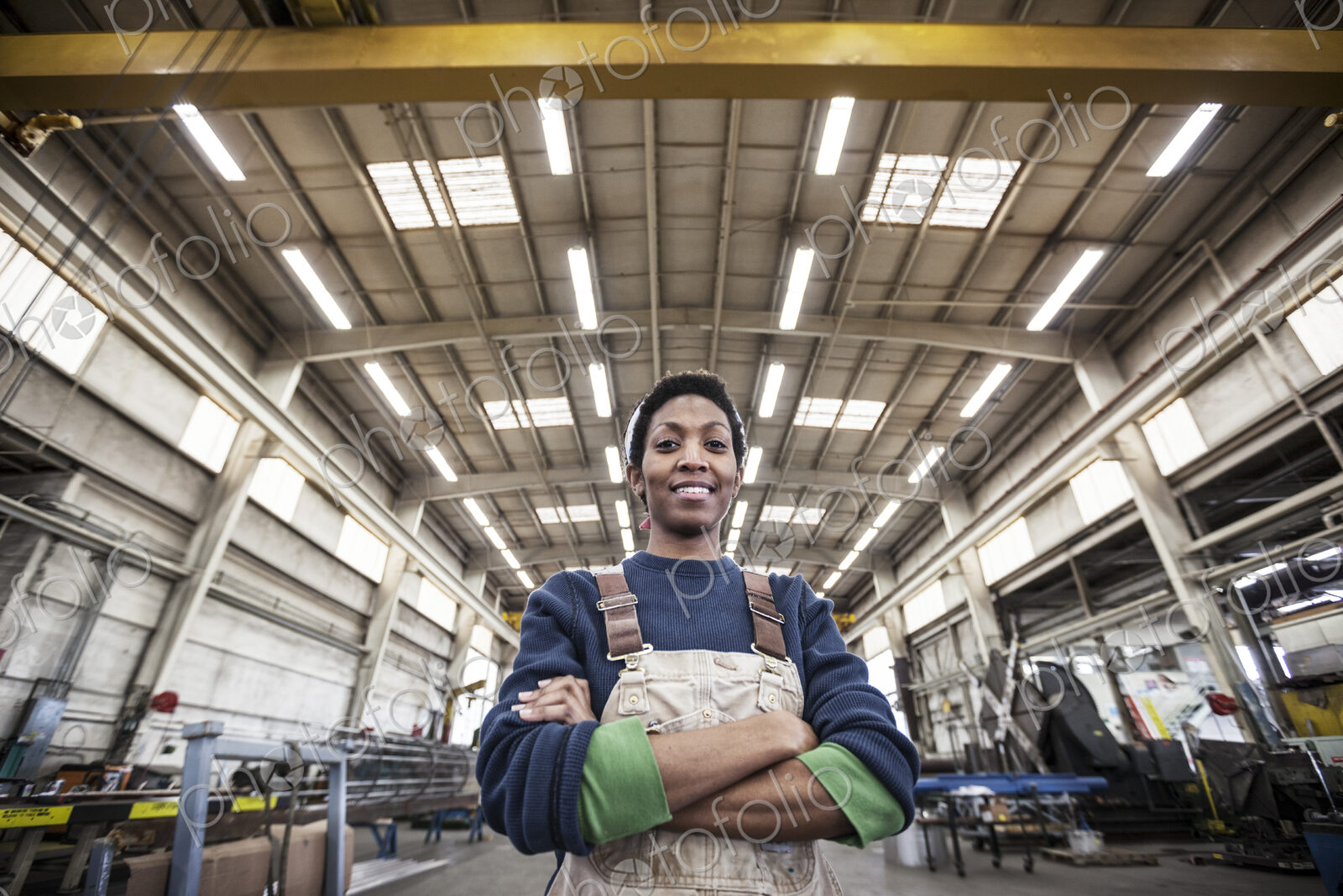 Black woman factory worker wearing coveralls in a large sheet metal factory.