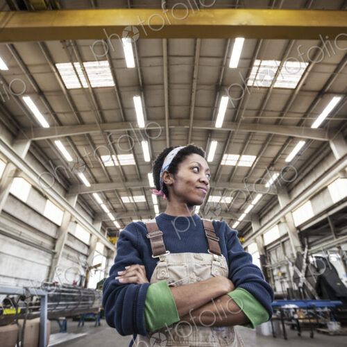 Black woman factory worker wearing coveralls in a large sheet metal factory.