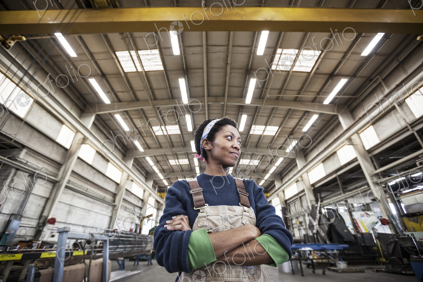 Black woman factory worker wearing coveralls in a large sheet metal factory.