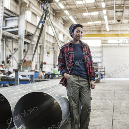 Black woman sitting next to a lift with aluminum pipes in a sheet metal factory. Black woman sitting next to a lift with aluminum pipes in a sheet metal factory.