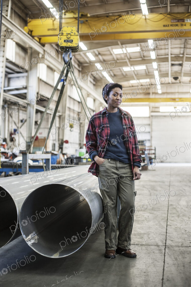 Black woman sitting next to a lift with aluminum pipes in a sheet metal factory.
