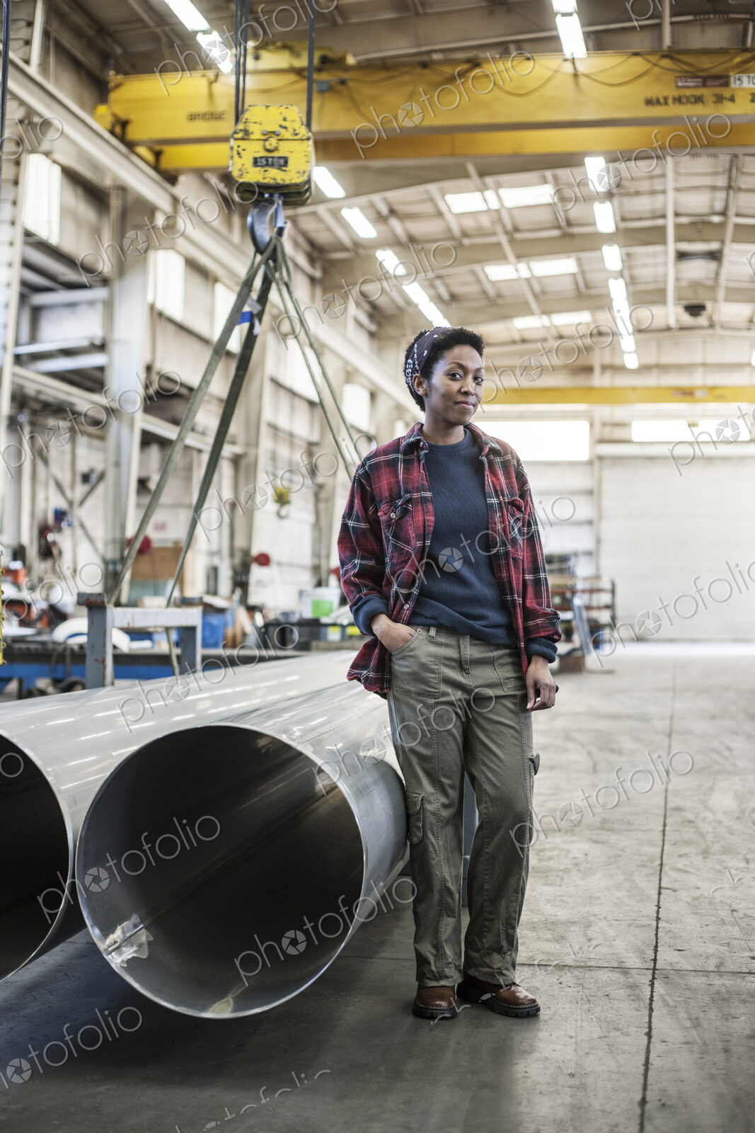 Black woman sitting next to a lift with aluminum pipes in a sheet metal factory.