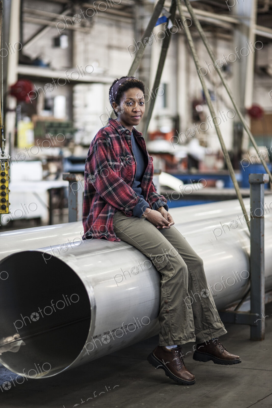 Black woman sitting next to a lift with aluminum pipes in a sheet metal factory.