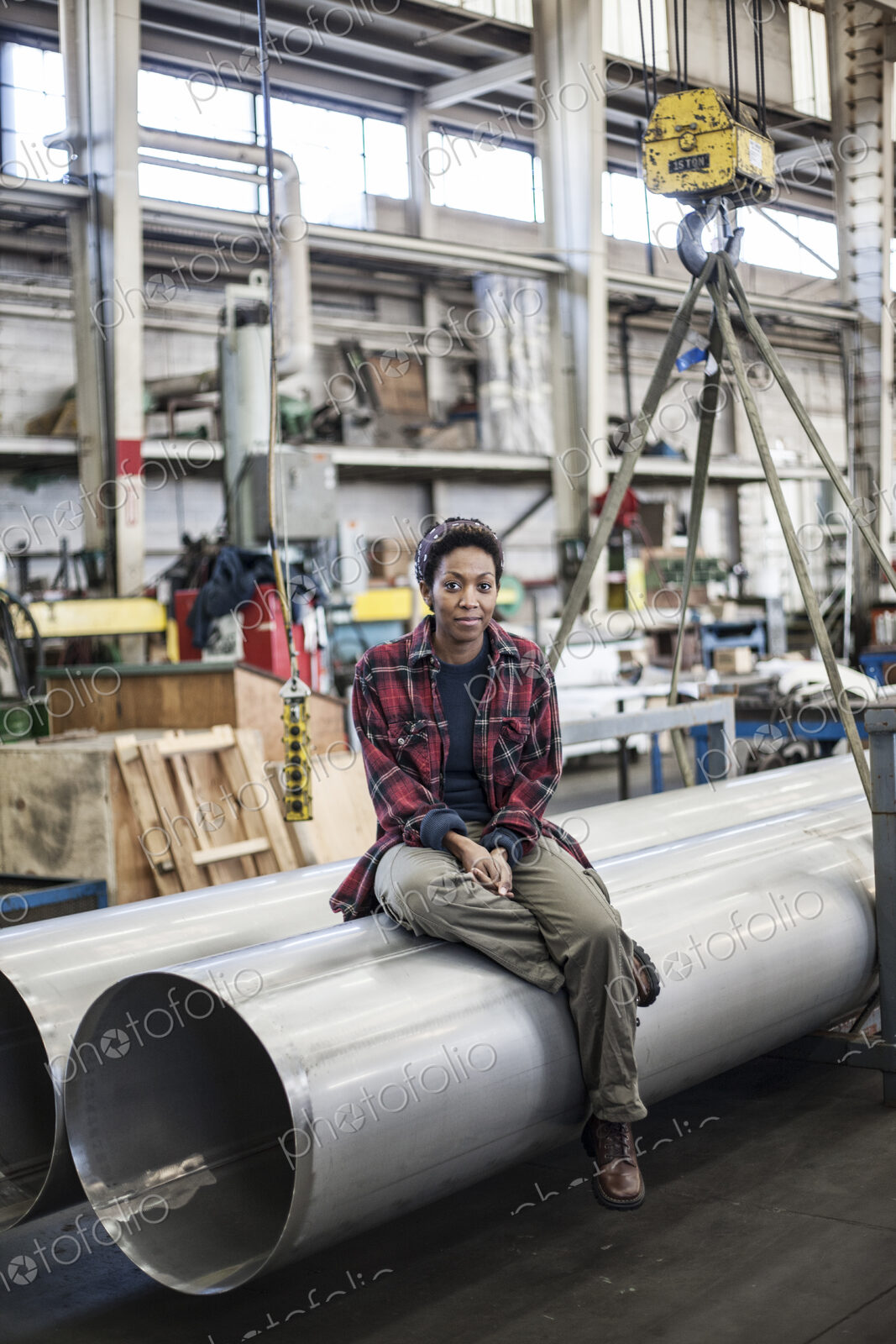 Black woman sitting next to a lift with aluminum pipes in a sheet metal factory.