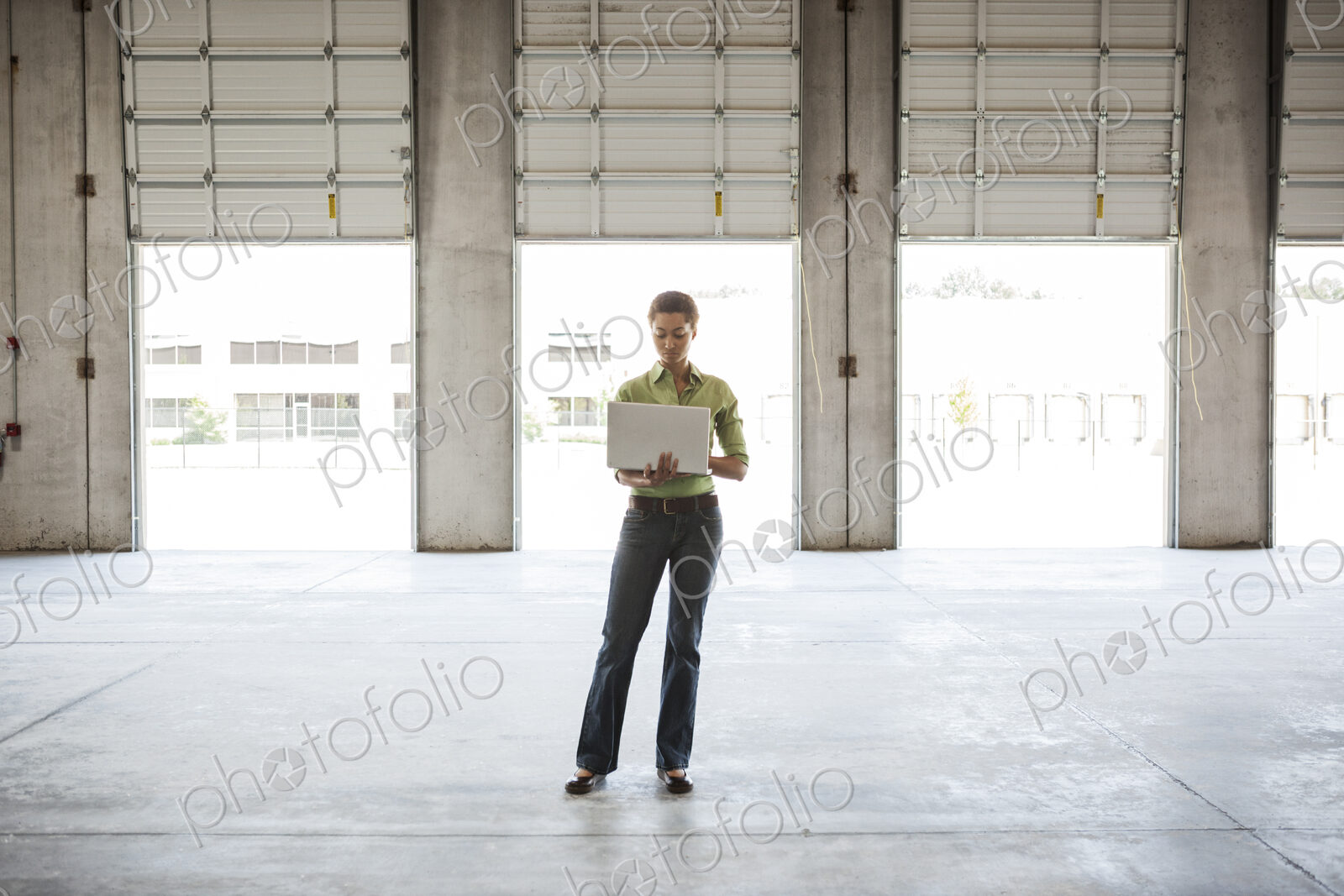 Black woman standing in front of new warehouse loading dock doors and using a lap top…
