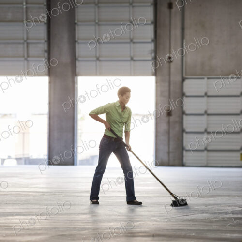 Black woman sweeping up in an empty warehouse space.
