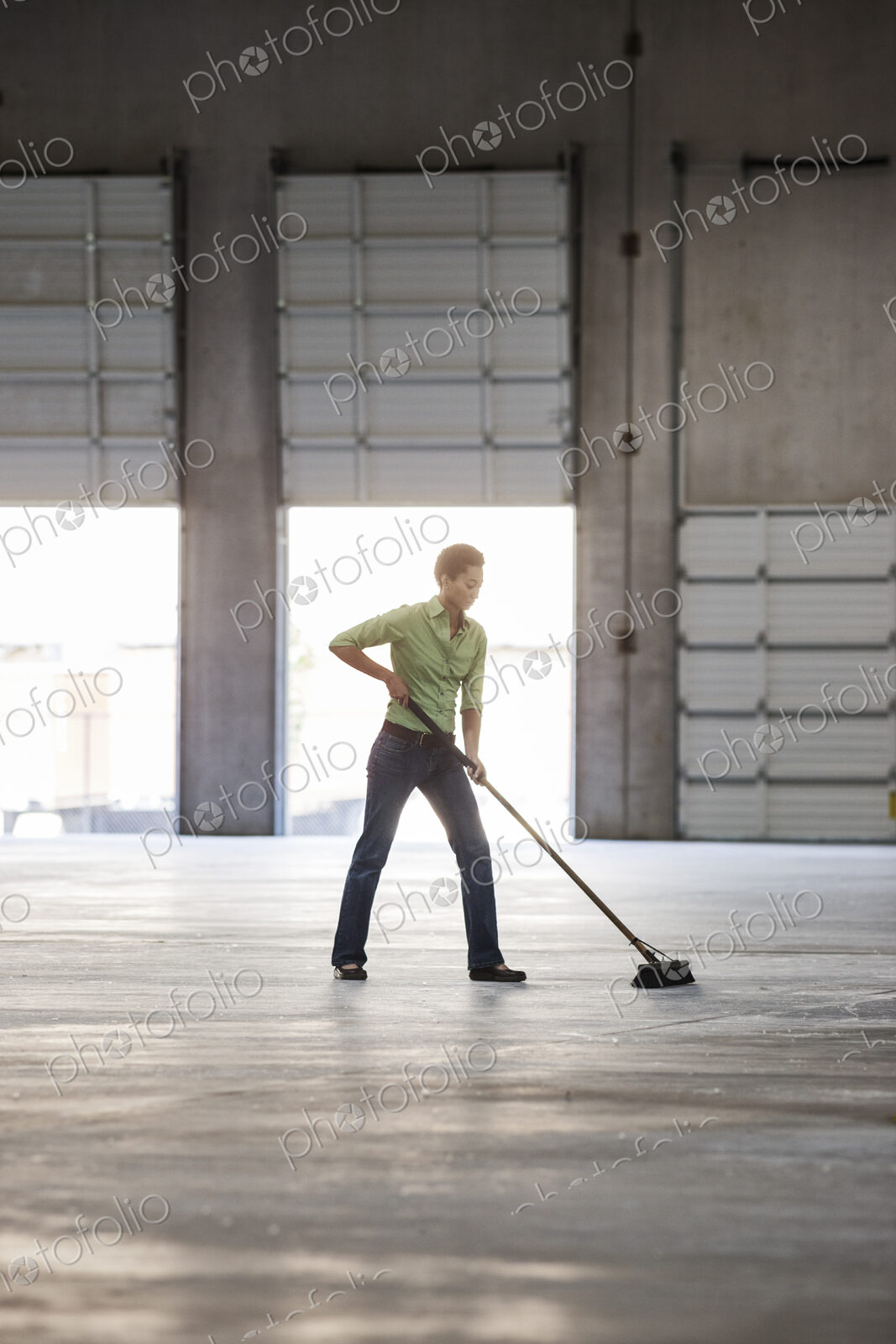 Black woman sweeping up in an empty warehouse space.