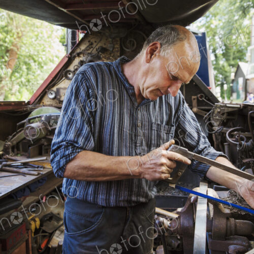 Blacksmith in his workshop on a working barge, at a work bench using a hacksaw.