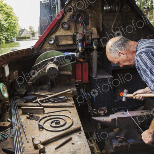 Blacksmith working in a small space on his narrowboat, a barge on river, bending over… Blacksmith working in a small space on his narrowboat, a barge on river, bending over…