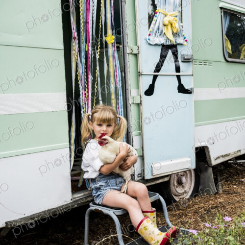 Blond girl holding white chicken sitting outside a caravan. Blond girl holding white chicken sitting outside a caravan.