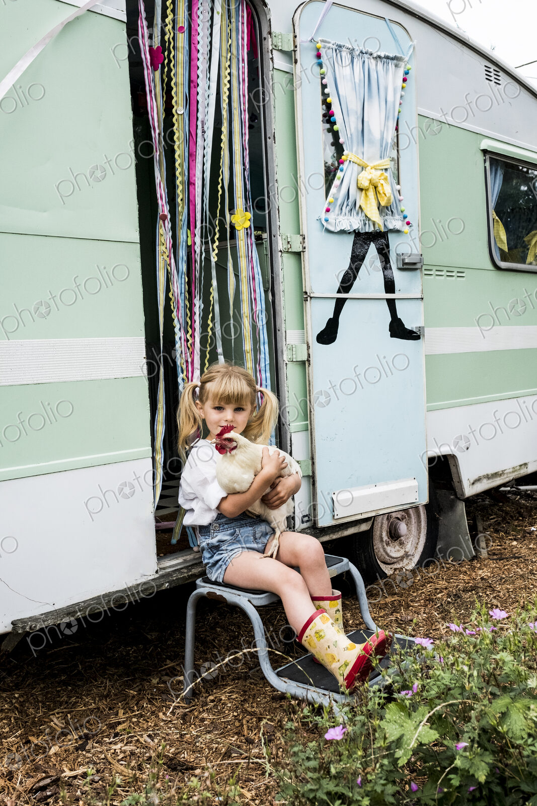 Blond girl holding white chicken sitting outside a caravan.