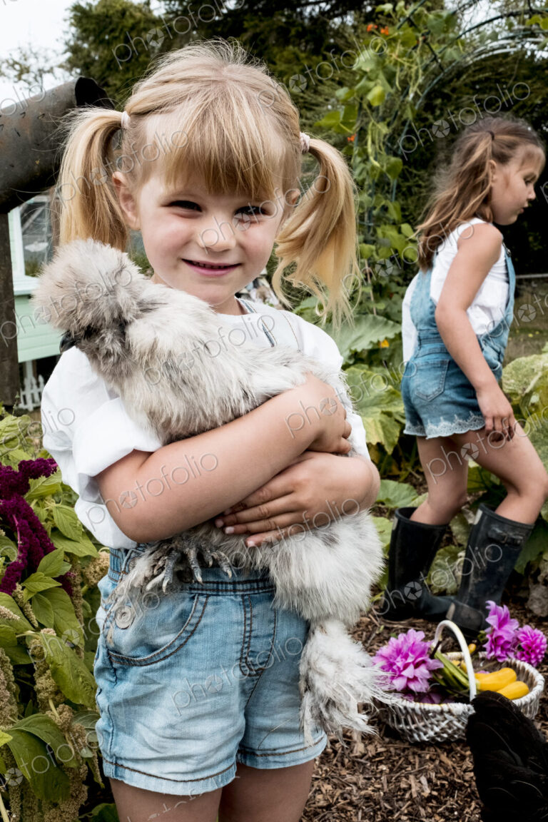 Blond girl standing in a garden, holding fluffy grey chicken.