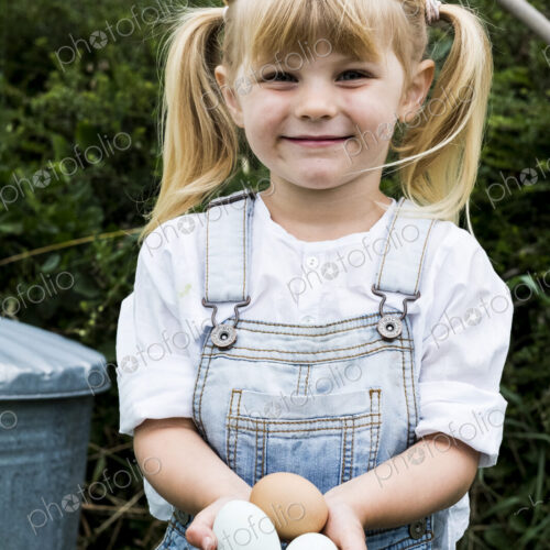 Blond girl standing in a garden, holding fresh eggs, smiling at camera. Blond girl standing in a garden, holding fresh eggs, smiling at camera.