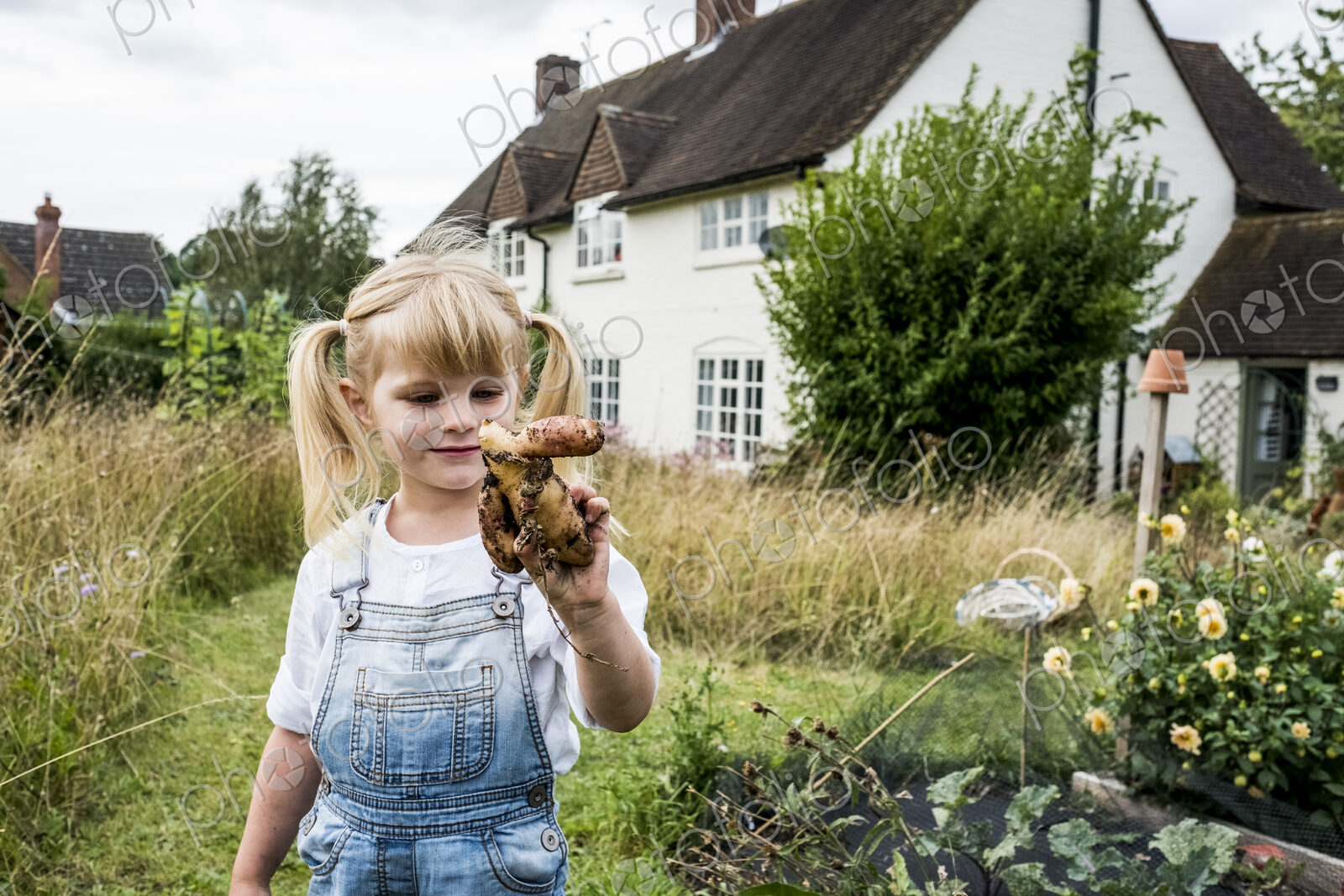 Blond girl standing in a garden, holding knobbly potato.
