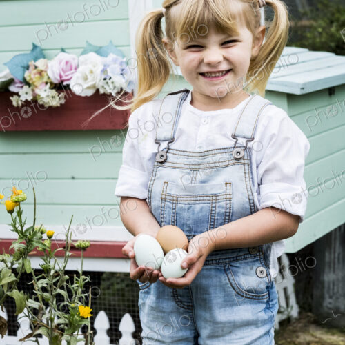 Blond girl standing in a garden in front of hen house, holding fresh eggs. Blond girl standing in a garden in front of hen house, holding fresh eggs.