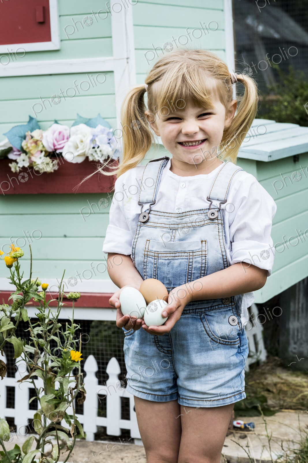 Blond girl standing in a garden in front of hen house, holding fresh eggs.