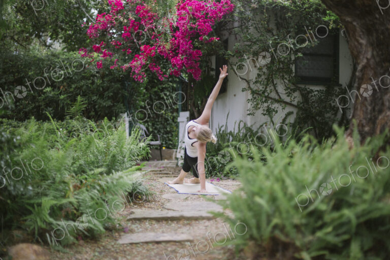 Blond woman doing yoga in a garden.
