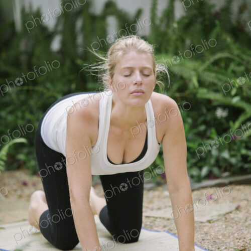 Blond woman doing yoga in a garden.