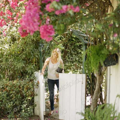 Blond woman entering a garden through a white wooden gate. Blond woman entering a garden through a white wooden gate.