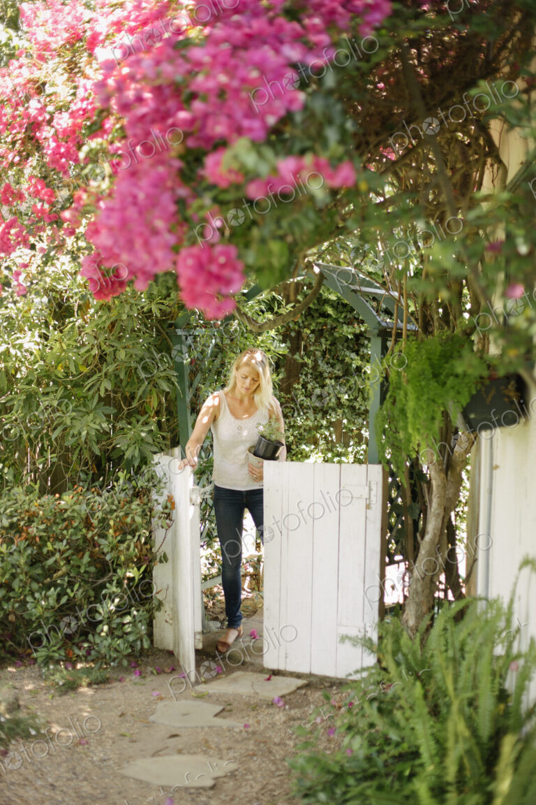 Blond woman entering a garden through a white wooden gate.