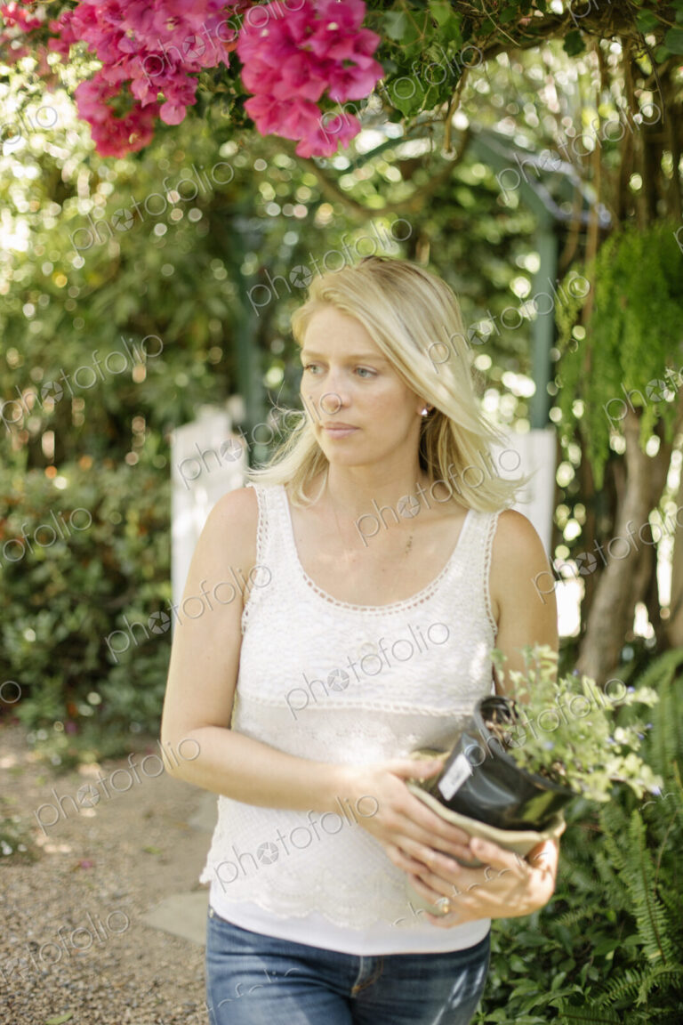 Blond woman in a garden, holding a plant pot.